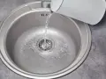 Woda leje się do metalowej komory zlewu z białego czajnika.