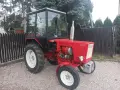 Czerwony traktor T-25 z kabiną stoi na żwirowym podwórku.