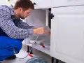 Hydraulik naprawia rury pod zlewem w kuchni.