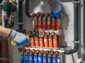 Hydraulik w rękawiczkach dokręca kluczem instalację z rurkami grzewczymi.