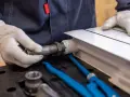 Hydraulik w białych rękawiczkach dokręca metalową rurę do białego grzejnika.