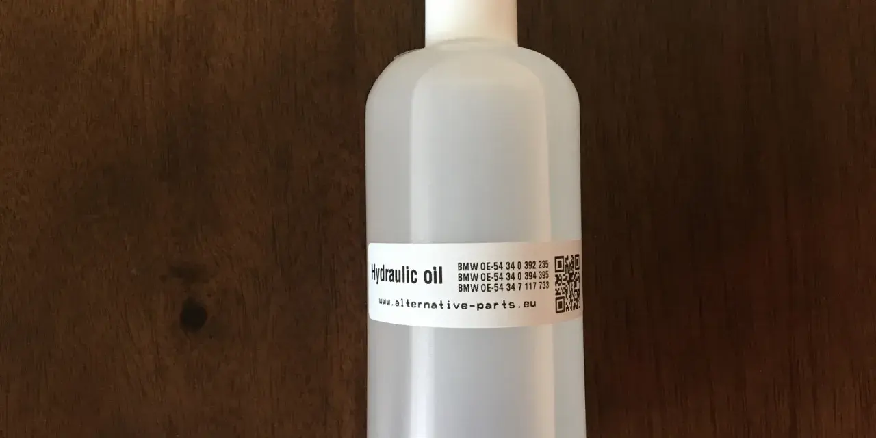 Biała butelka z olejem hydraulicznym na drewnianym tle.