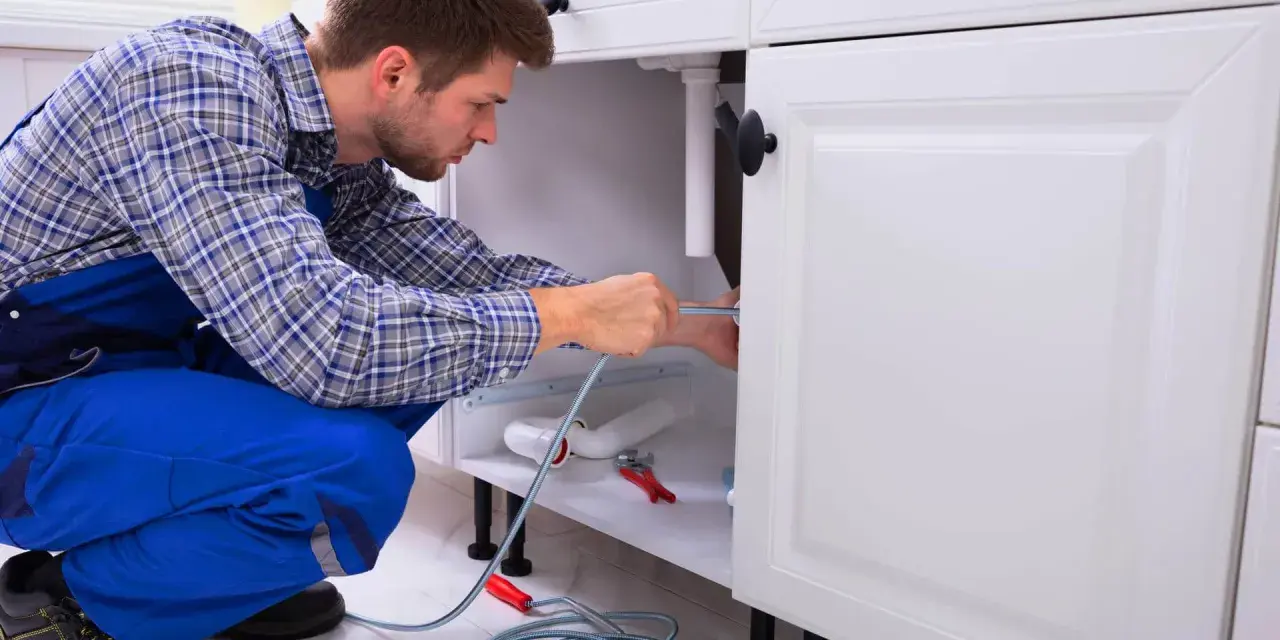 Hydraulik naprawia rury pod zlewem w kuchni.