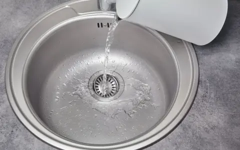 Woda leje się do metalowej komory zlewu z białego czajnika.