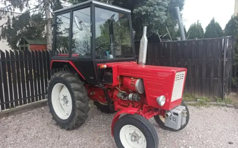 Czerwony traktor T-25 z kabiną stoi na żwirowym podwórku.
