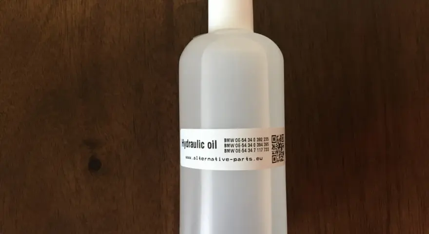 Biała butelka z olejem hydraulicznym na drewnianym tle.
