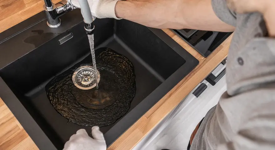 Ręce w rękawiczkach udrażniają zatkany zlew, z którego leje się woda.